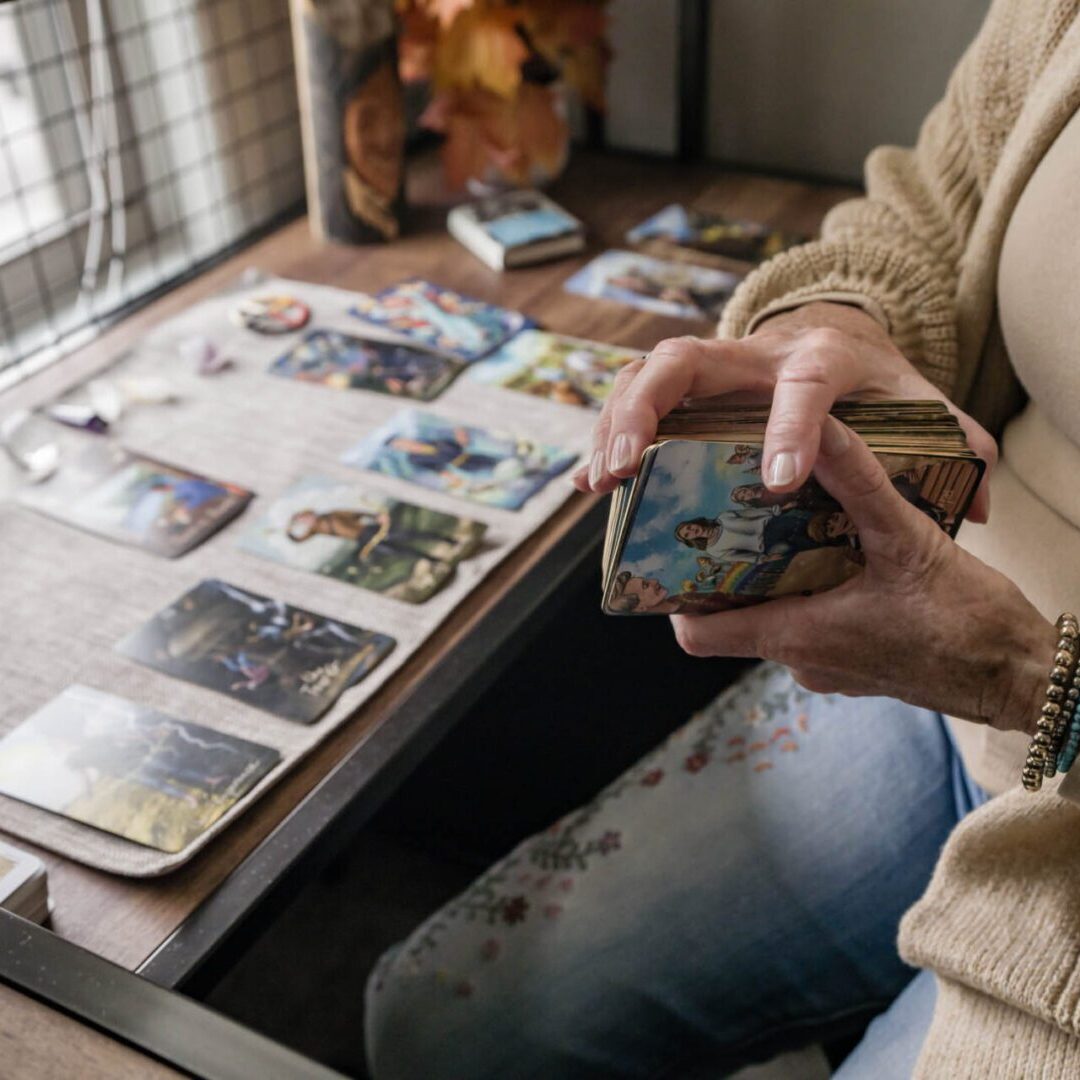 Person organizing tarot cards on a table with a book nearby.